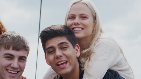 Outdoor-Portrait-Of-Student-Friends-With-Men-Giving-Women-Piggyback-Rides