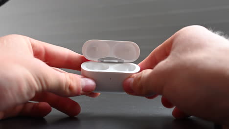 un joven aficionado a la música hace girar entre sus dedos una caja blanca que contiene auriculares para entretenerse