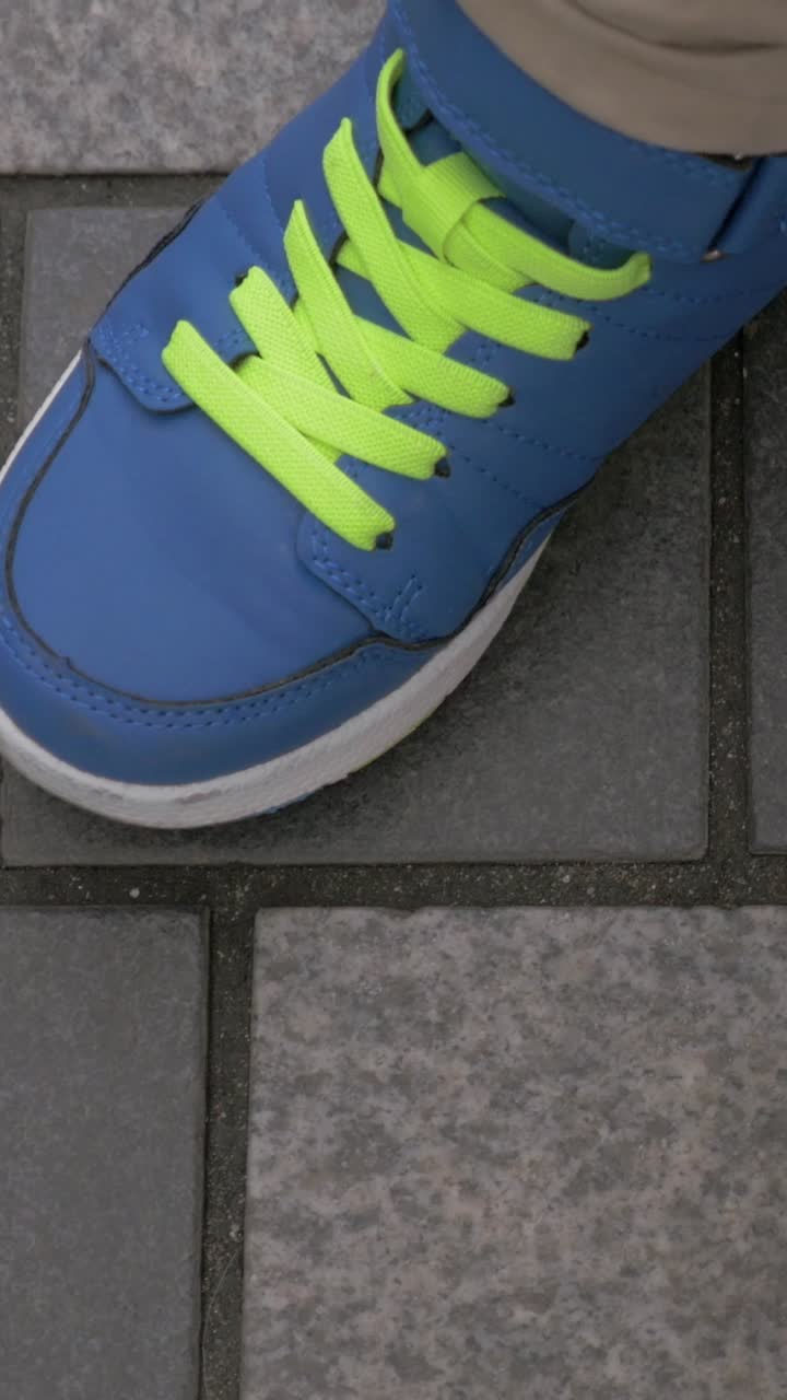 Child's Feet in Blue Sneakers with Bright Green Laces on Pavement