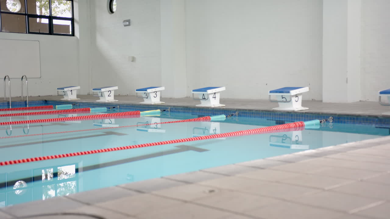 Empty indoor swimming pool with starting blocks and lane dividers, copy space