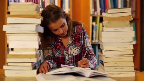 estudiante atento estudiando y tomando notas en la biblioteca rodeado de libros