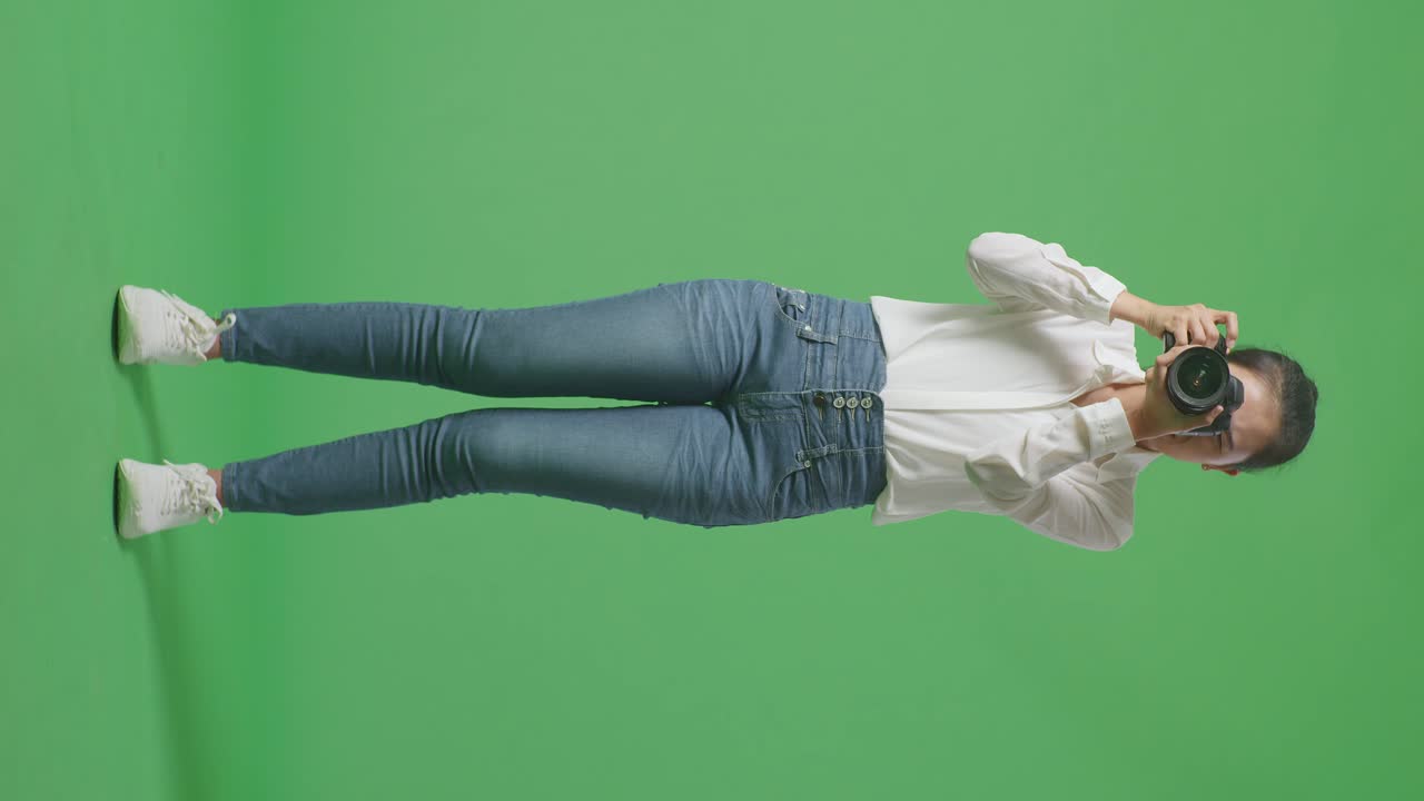 분노한 아시아 사진작가의 몸은 스튜디오에서 녹색 화면 배경에서 카메라로 사진을 찍는 동안 모델에게 왼쪽과 오른쪽으로 움직이라고 말합니다.