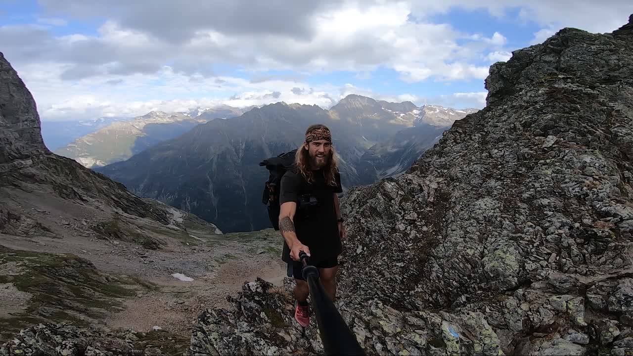 un hombre joven y en forma con cabello largo y tatuajes está dando un paso hacia el borde de un acantilado empinado en la cima de una montaña en suiza