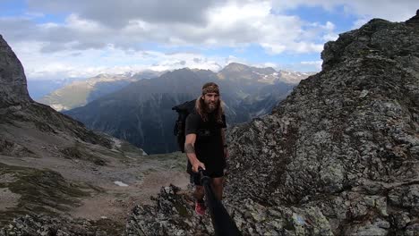 A-young,-fit-man-with-long-hair-and-tattoos-is-taking-a-step-out-onto-the-edge-of-a-steep-cliff-on-top-of-a-mountain-in-Switzerland