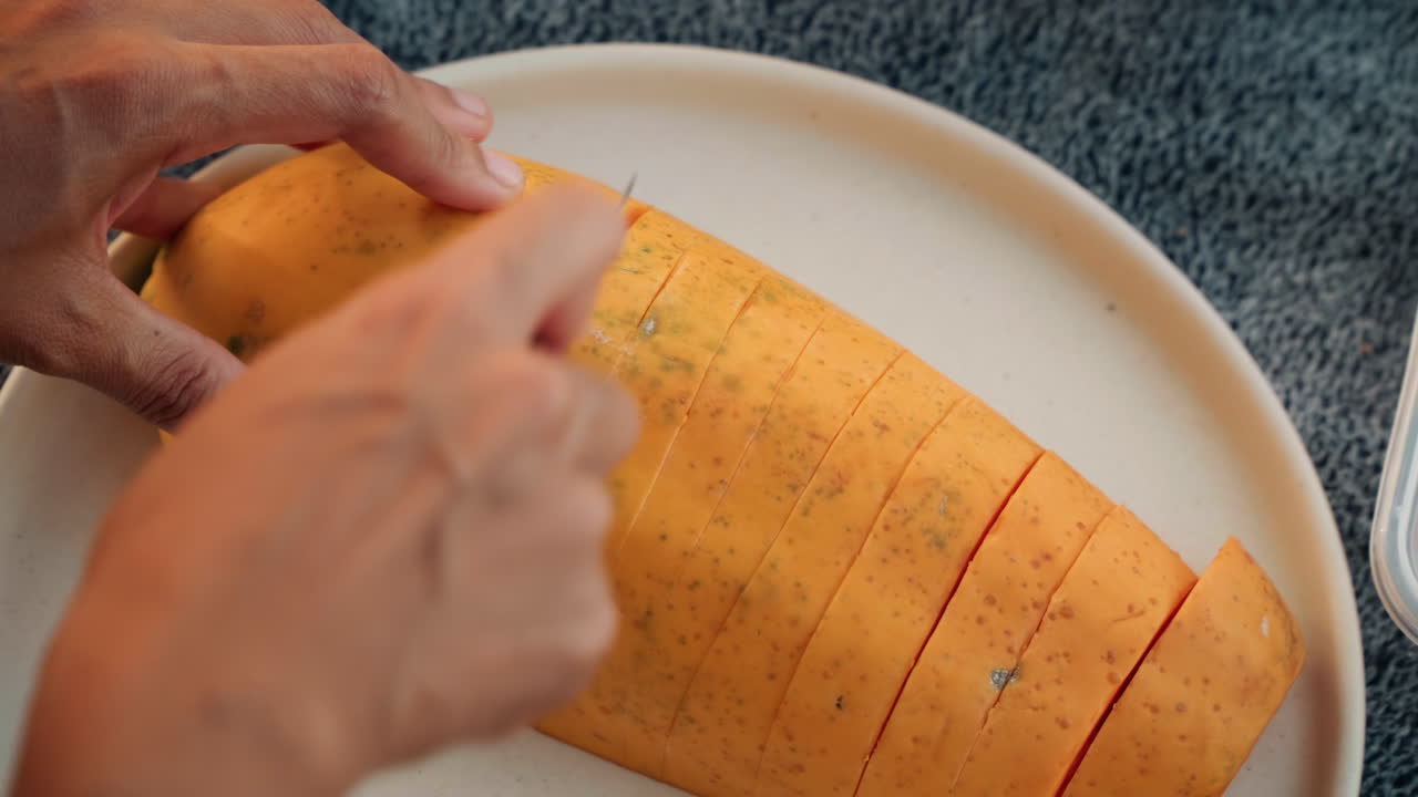 Hands slicing papaya on plate during intimate beach tea ceremony, couple preparing fresh tropical snack on towel with knife and tray, warm sunlight, closeup of texture and seeds, calm seaside