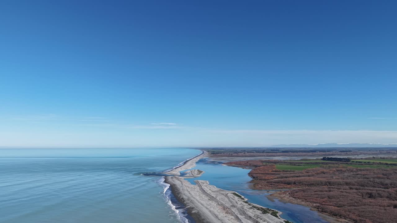High aerial reverse (wide view) above beautiful turquoise colored South Pacific Ocean with Rakaia Lagoon, River and farmland on a clear winter's day (Canterbury, New Zealand)