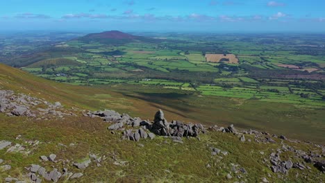 aerial orbit view of rock outcrop, ridge line and valley with view into the distance over the south of ireland farmland