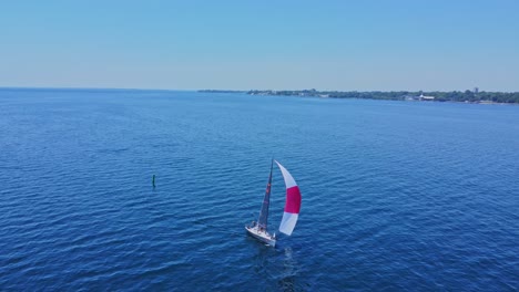 aerial small sailboat out in the open water on a blue sky day