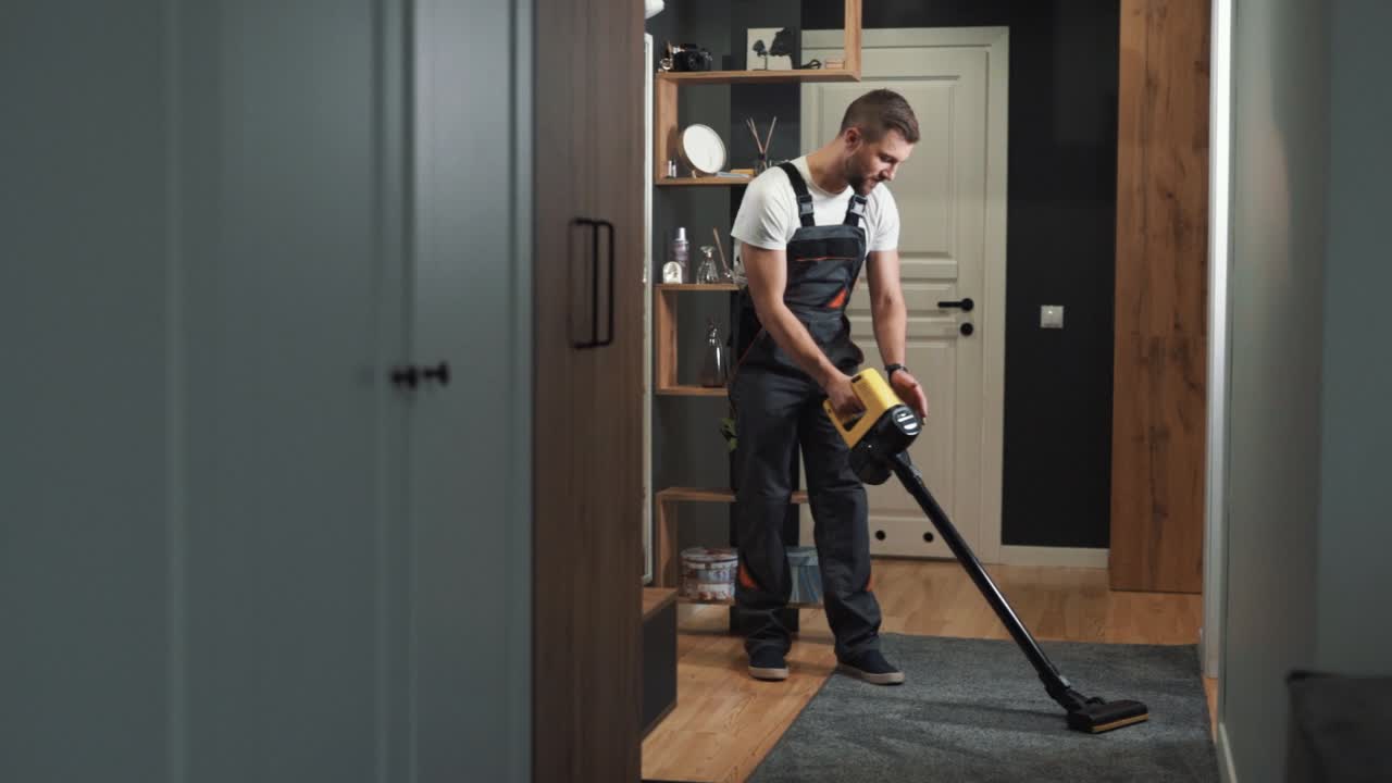 un limpiador profesional masculino limpia una alfombra con una aspiradora inalámbrica