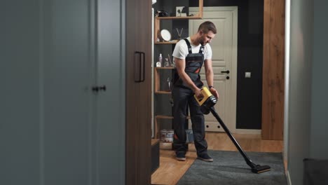 a male professional cleaner cleans a carpet with a cordless vacuum cleaner