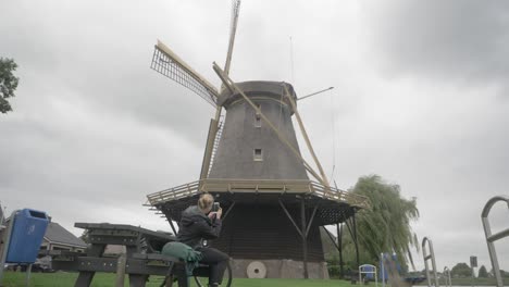 Turismo-En-Los-Países-Bajos---Una-Joven-Sentada-Toma-Una-Foto-De-Un-Viejo-Molino-De-Viento