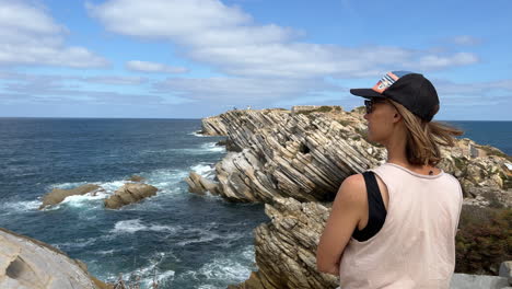 Woman-standing-on-a-cliff-looking-at-the-ocean-on-a-windy-day