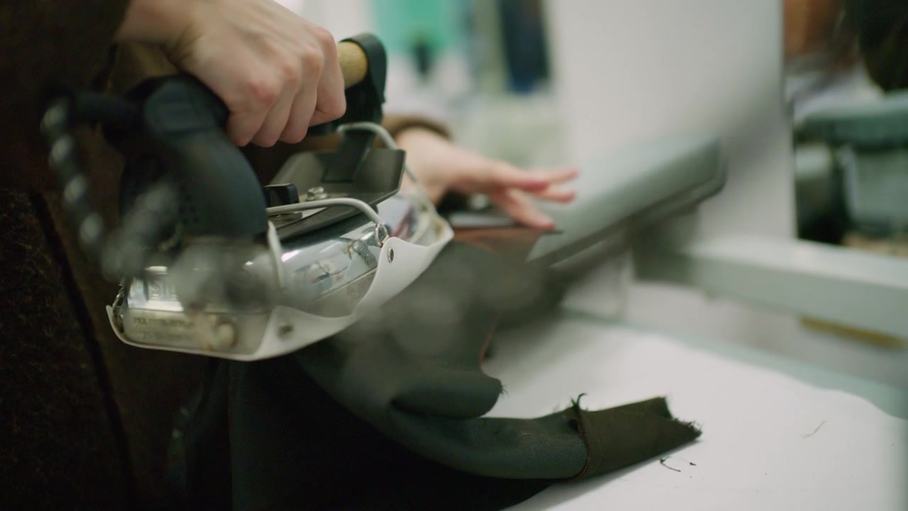 Close up of a tailor using a professional steam iron on black fabric in a fashion workshop