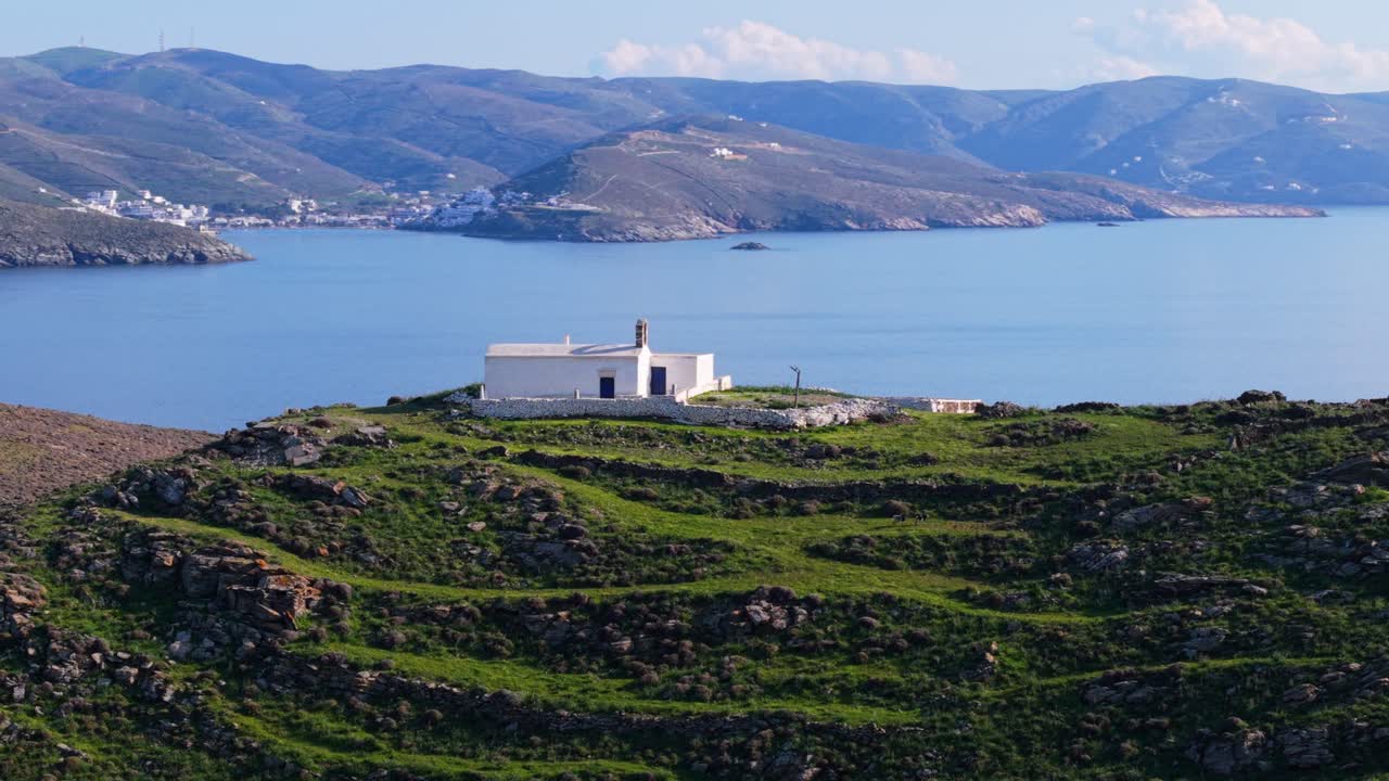 Panoramic drone over green hills and sacred church on Kythnos island during clear sunny day