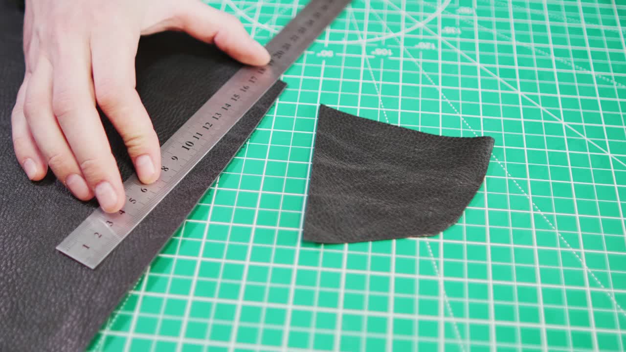 Um artesão de couro mede e corta o material com cuidado. O processo inclui o uso de ferramentas para criar formas precisas. Isso demonstra as etapas importantes no trabalho com couro.