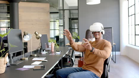 using vr headset, african american man sitting at desk in modern office, smiling and interacting