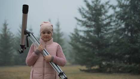 Kid-interested-in-astronomy-and-science-with-telescope-in-the-nature,-looking-at-camera