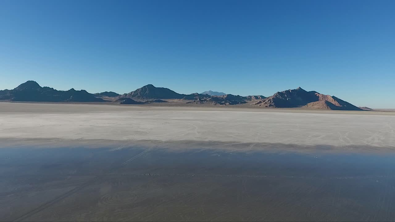 Uma imagem aérea de drone revela água calma cobrindo o sal branco das Planícies Salgadas de Bonneville e montanhas distantes