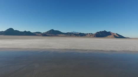 An-aerial-drone-shot-reveals-smooth-water-covering-the-white-salt-of-the-Bonneville-Salt-Flats-and-distant-mountains