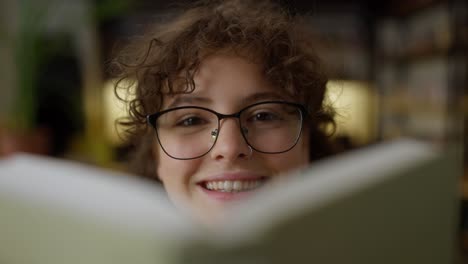 Primer-Plano-De-Una-Chica-Segura-De-Sí-Misma,-Con-Cabello-Rizado-Y-Gafas,-Leyendo-Un-Libro-En-La-Biblioteca.