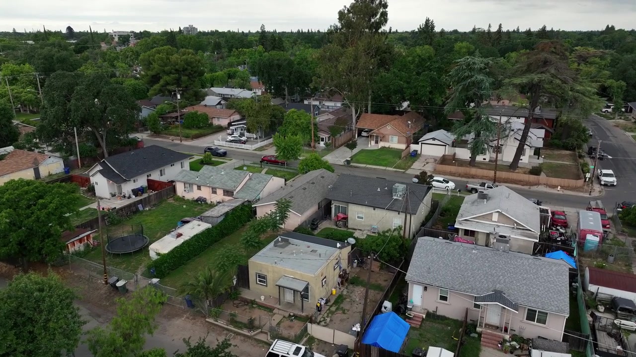Residential neighborhood in Modesto, California with modest homes, narrow streets, parked cars and dense layout, everyday suburban living environment in Central Valley,United States. Aerial flyover.