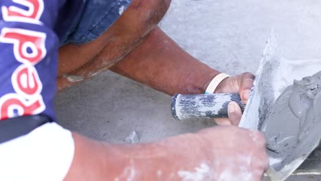 a person spreads cement on a surface outdoors, using a trowel, under bright daylight conditions