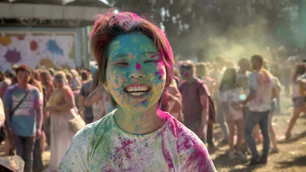 Giovane ragazza asiatica felice alza le mani al festival Holi di giorno in estate, guardando la fotocamera, concetto di colore, concetto emotivo