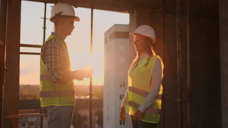 en cámara lenta de dos ingenieros están hablando sobre el futuro proyecto para la construcción de un rascacielos centro de negocios y estrechando la mano al atardecer.