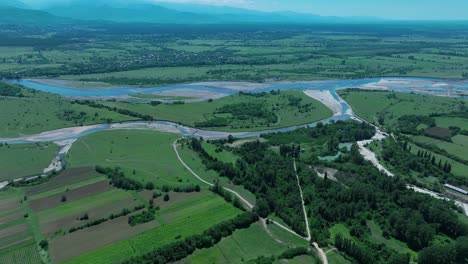 Aerial-view-of-a-river-bend-surrounded-by-green-fields-and-farmland,-illustrating-the-harmony-between-natural-water-bodies-and-agriculture