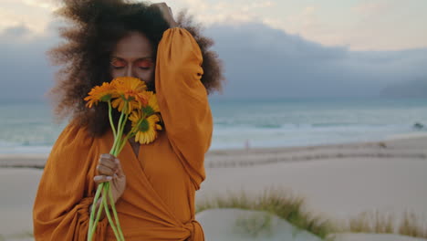 portrait girl posing seashore with orange flowers. woman sniffing cute bouquet