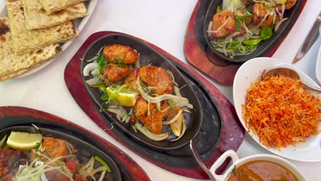 traditional indian tandoori chicken with onions on a very hot plate with steam smoke, butter chicken, cheese naan bread and coconut rice in a restaurant, authentic asian cuisine, 4k shot