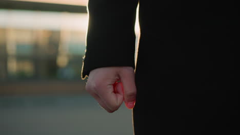 primer plano de una mano con una manga negra apretada en el puño, suavemente iluminada por la luz del sol dorada, con un fondo urbano borroso con tonos cálidos y luz reflectante