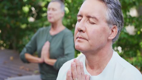 relaxed senior caucasian couple practicing yoga together and smiling sitting in garden