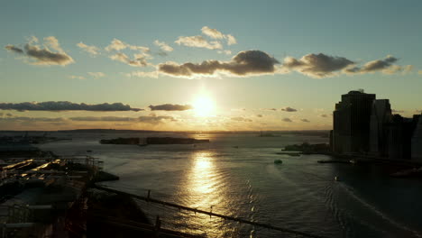 Backwards-reveal-of-silhouette-of-historic-cable-stayed-bridge-with-US-flag-on-top.-View-against-romantic-sunset.-Manhattan,-New-York-City,-USA