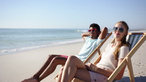 young biracial man and young caucasian woman relax on beach chairs by the sea