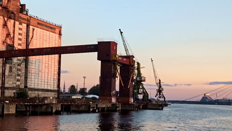 sunset over an industrial port with rusty cranes