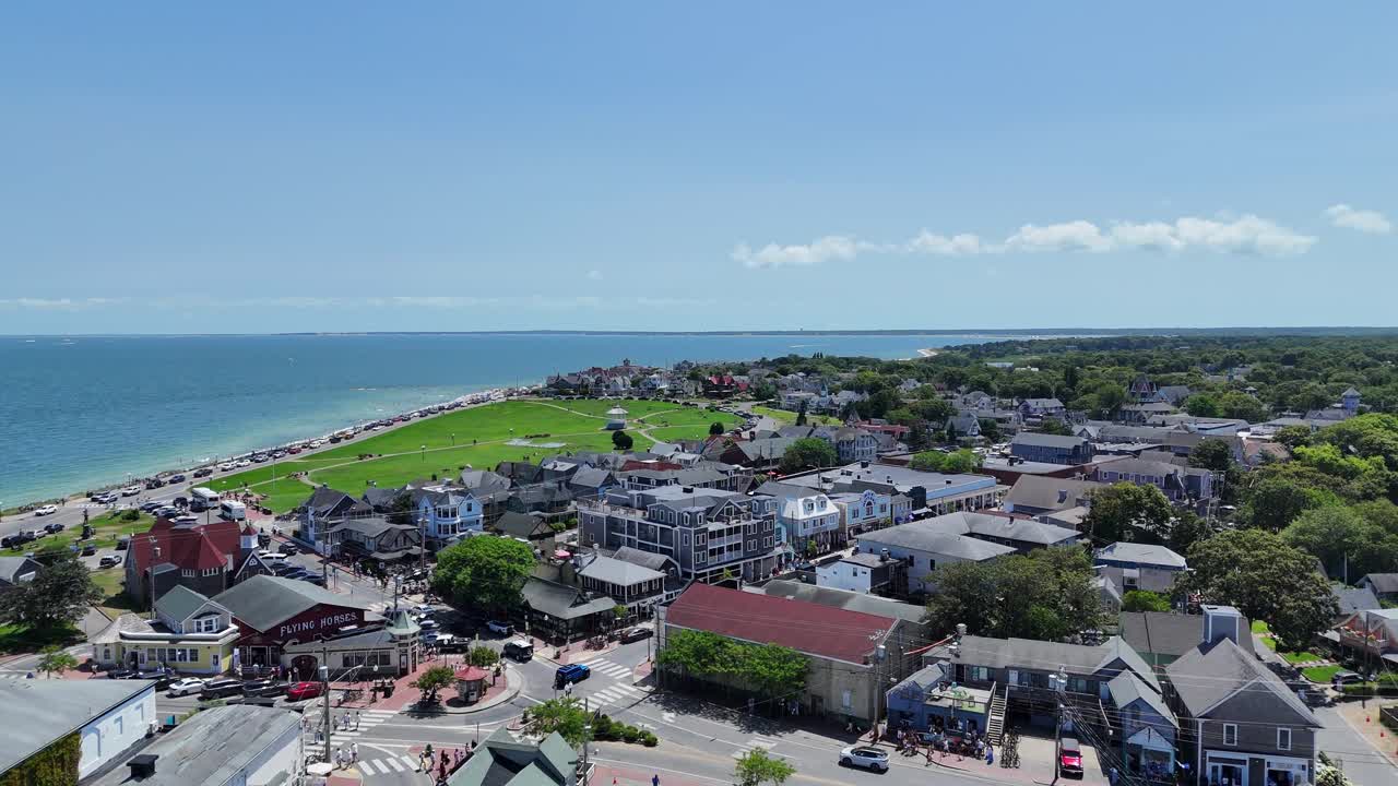 La città insulare di Martha’s Vineyard, nella Contea di Dukes, Massachusetts, che mostra un quartiere costiero, un porto turistico, case di lusso e la costa atlantica sotto cieli estivi luminosi. Una ripresa aerea con drone mostra l'erba nel parco.