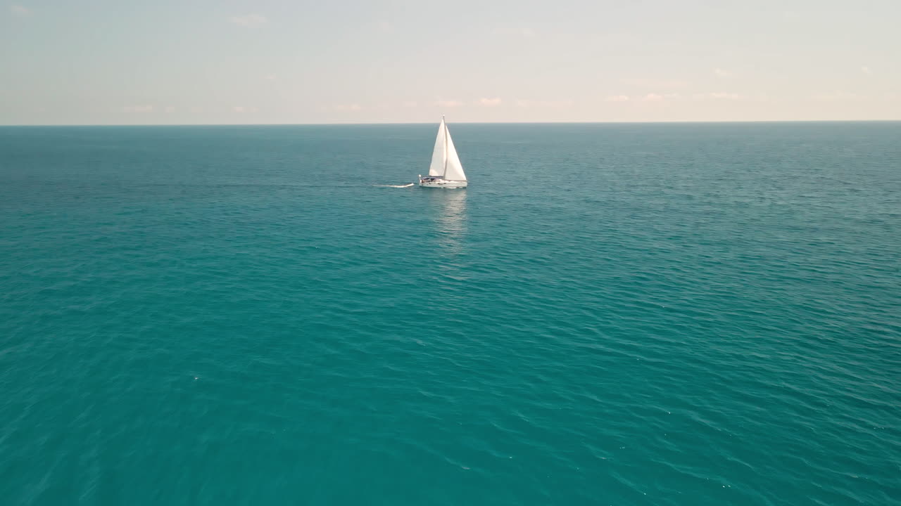 velero navegando por el océano azul - hermoso mar azul claro y tranquilo durante el verano en cerdeña, italia - toma aérea de drones