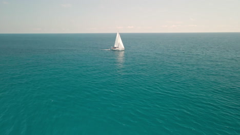 Velero-Navegando-Por-El-Océano-Azul---Hermoso-Mar-Azul-Claro-Y-Tranquilo-Durante-El-Verano-En-Cerdeña,-Italia---Toma-Aérea-De-Drones