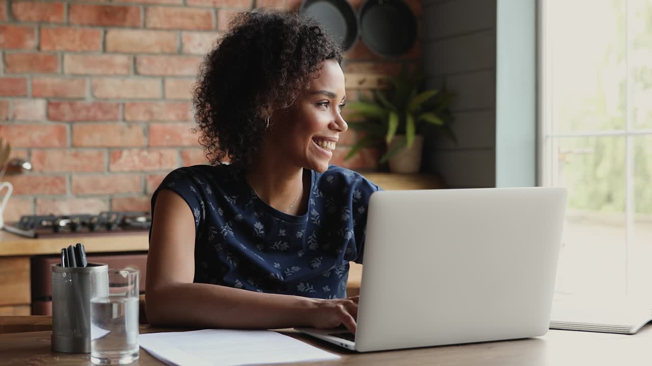joven africana feliz trabaja remotamente desde casa usando una computadora portátil