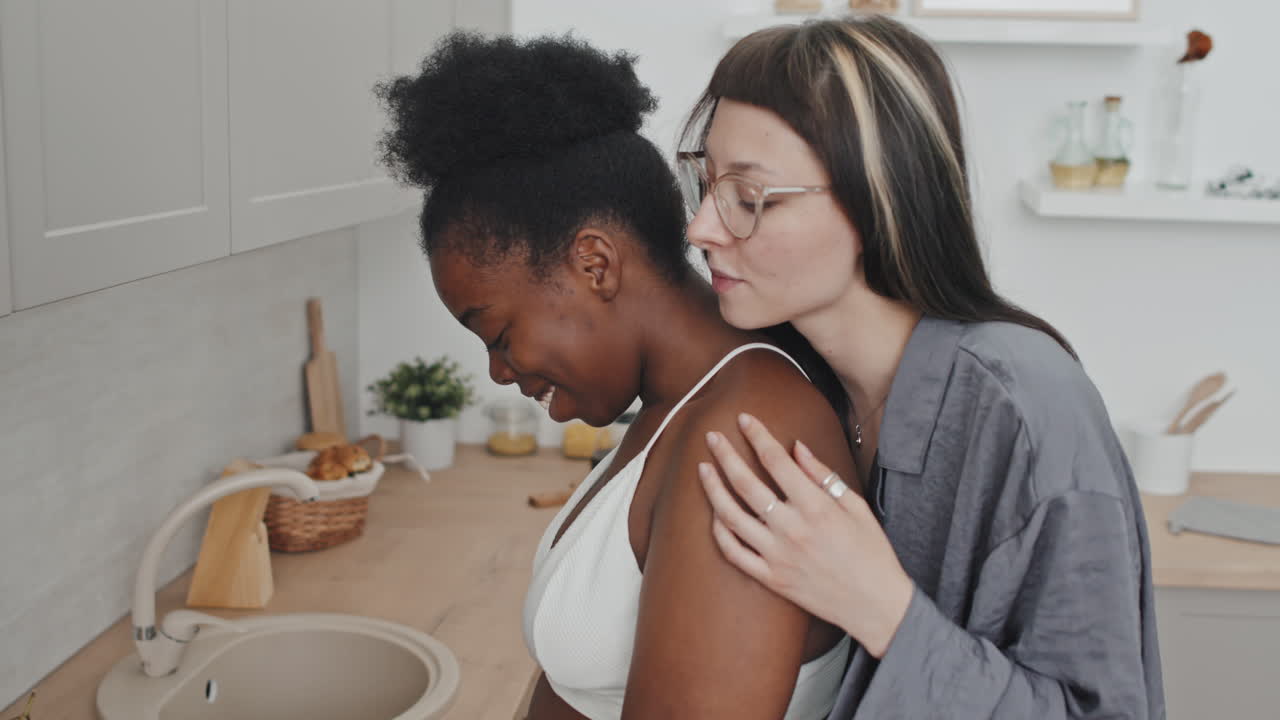 Woman Hugging Girlfriend Making Breakfast in Kitchen