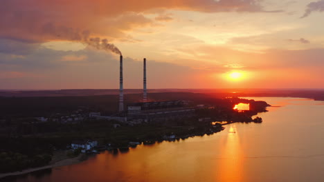 silhouette of a chemical plant near the river. industrial factory releases smoke at beautiful sunset time. dangerous manufacturing among nature. aerial view.