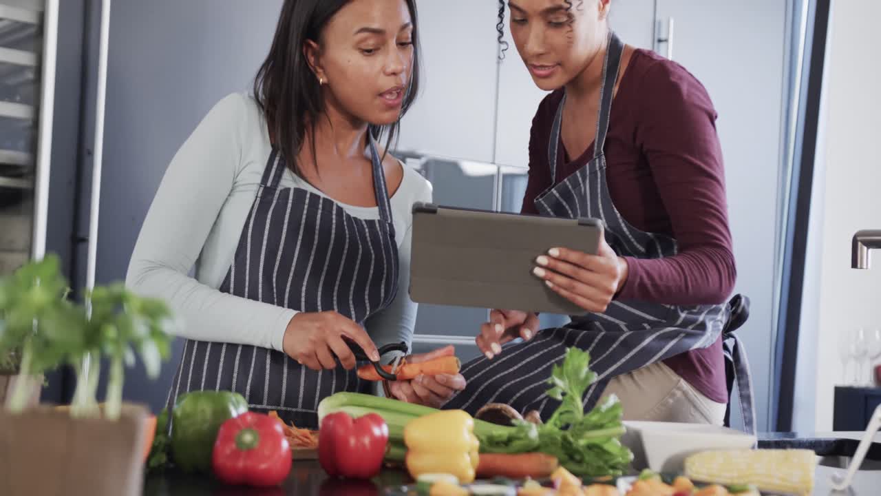 feliz pareja de lesbianas biraciales preparando verduras y usando tableta en la cocina, en cámara lenta