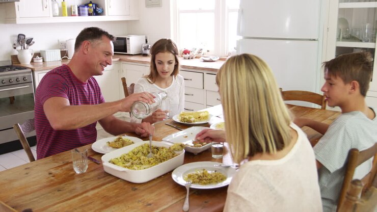Family With Teenage Children Eating Meal Around Table In Kitchen