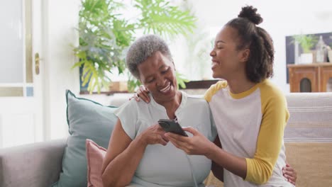 African-american-mother-and-daughter-smiling-while-using-smartphone-together-at-home