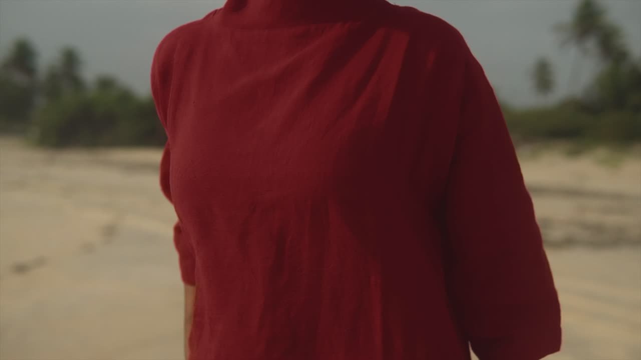 confundida mujer bruneta india con vestido rojo de pie en la playa mira a su alrededor, estando molesta