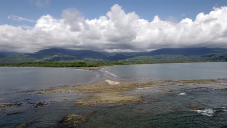 Vista-De-Drones-De-Olas-Rompiendo-En-La-Playa-Con-Cielo-Azul-Y-Nubes-Blancas-A-La-Deriva