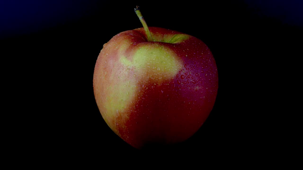 Red-yellow organic apple rotates around slowly on black background.