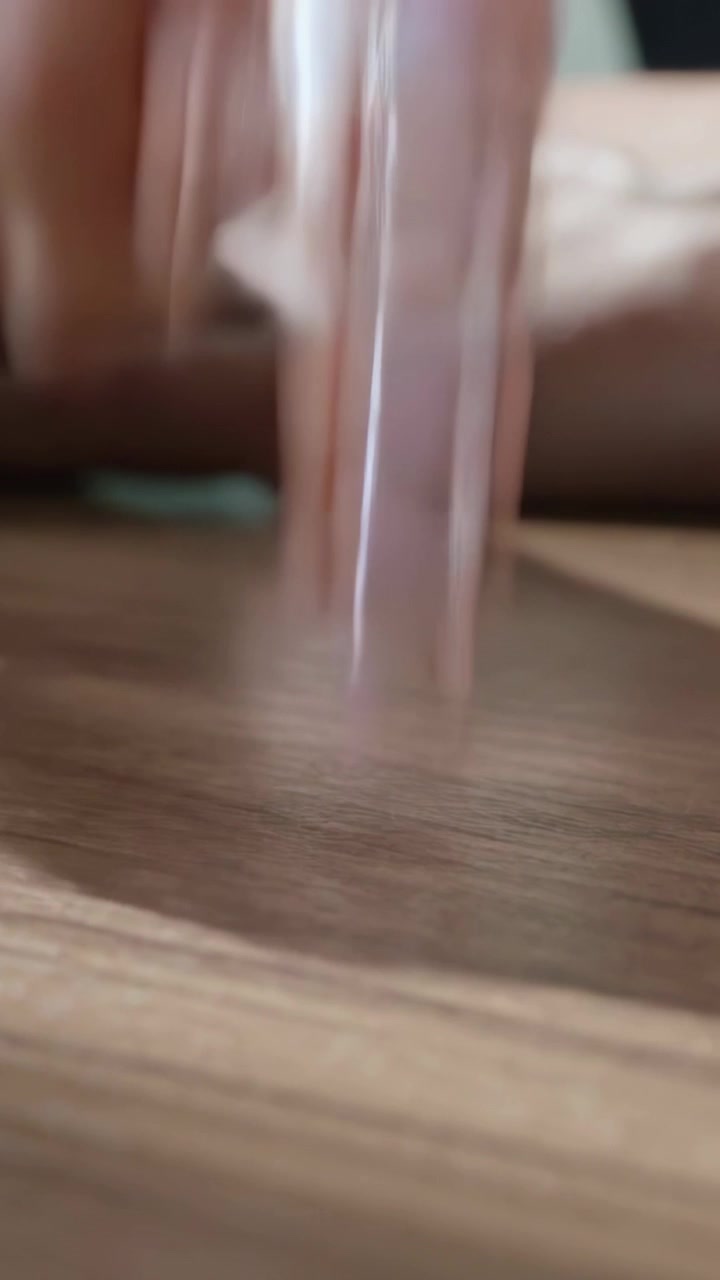 Vídeo vertical: Ponta do dedo com manicure deslizando sobre um tampo de mesa com padrão de madeira, verificando o brilho do esmalte.