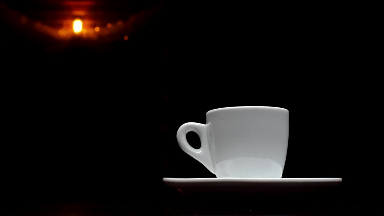 Una tazza di caffè caldo su sfondo nero con una lampada sullo sfondo in risoluzione 4K